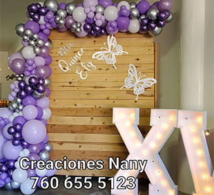 Decorative setup with lit "XI" letters, balloon arch, and wooden backdrop for an event.