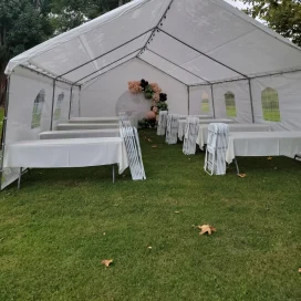 White event tent with chairs and tables on a grassy area, adorned with a balloon arch inside.