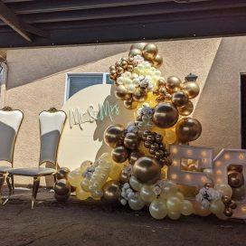 Two ornate chairs beside "Mr & Mrs" sign and balloon arrangement with illuminated "50" decor.