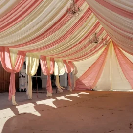 Elegant draped ceiling and walls in pink, cream, and yellow hues inside a tent.