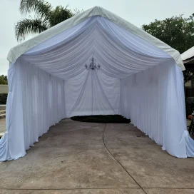 Elegant white draped canopy tent with chandelier, set up outdoors.