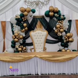 Elegant event setup with a white royal chair and balloon arch in gold, white, and green.