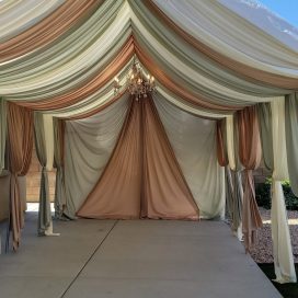 Elegant tent interior with draped cream and beige fabric and a chandelier, under a clear sky.