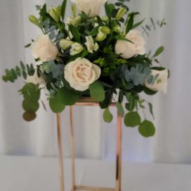 A bouquet of cream roses on a gold geometric stand.