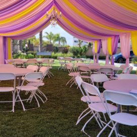 Outdoor event space with pink and yellow drapery and rows of white chairs under a tent.