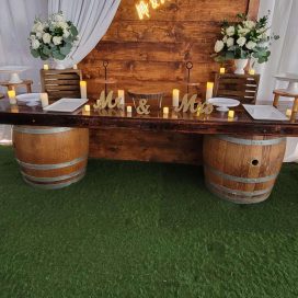 Rustic wedding sweetheart table with "Mr & Mrs" sign, neon "love" backdrop, candles, and floral arrangements.