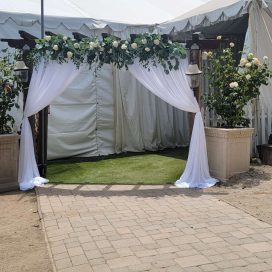 Decorated entrance to a white tent with drapes and flowers, set on a brick pathway.