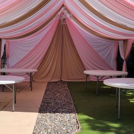 Elegant pink and white draped tent with tables for an event, clear blue sky above.