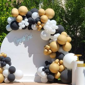 Outdoor graduation party setup with a balloon arch and "Congrats Grad" backdrop.