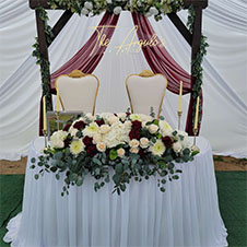 Wedding setup with white draped arch, floral decoration, and elegant chairs.