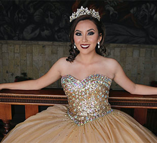 Person in a bedazzled gold ball gown with a tiara, sitting on a bench.